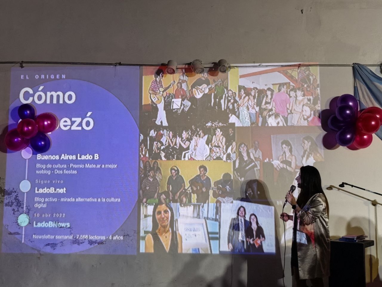 Irina Sternik hablando con micrófono junto a los globos, con la placa del origen de LadoBNews proyectada